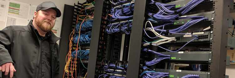 An engineer beside racks of network switches and patch cabling